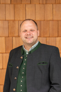 Lächelnder Mann in Tracht vor Holzwand, regionale Lebensmittel Lungau, bäuerlicher Betrieb