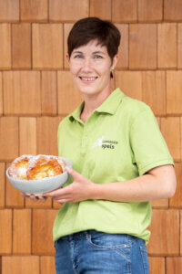 Frau im grünen Lungauer Speis Polo hält Schüssel mit regionalem Gebäck vor Holzwand